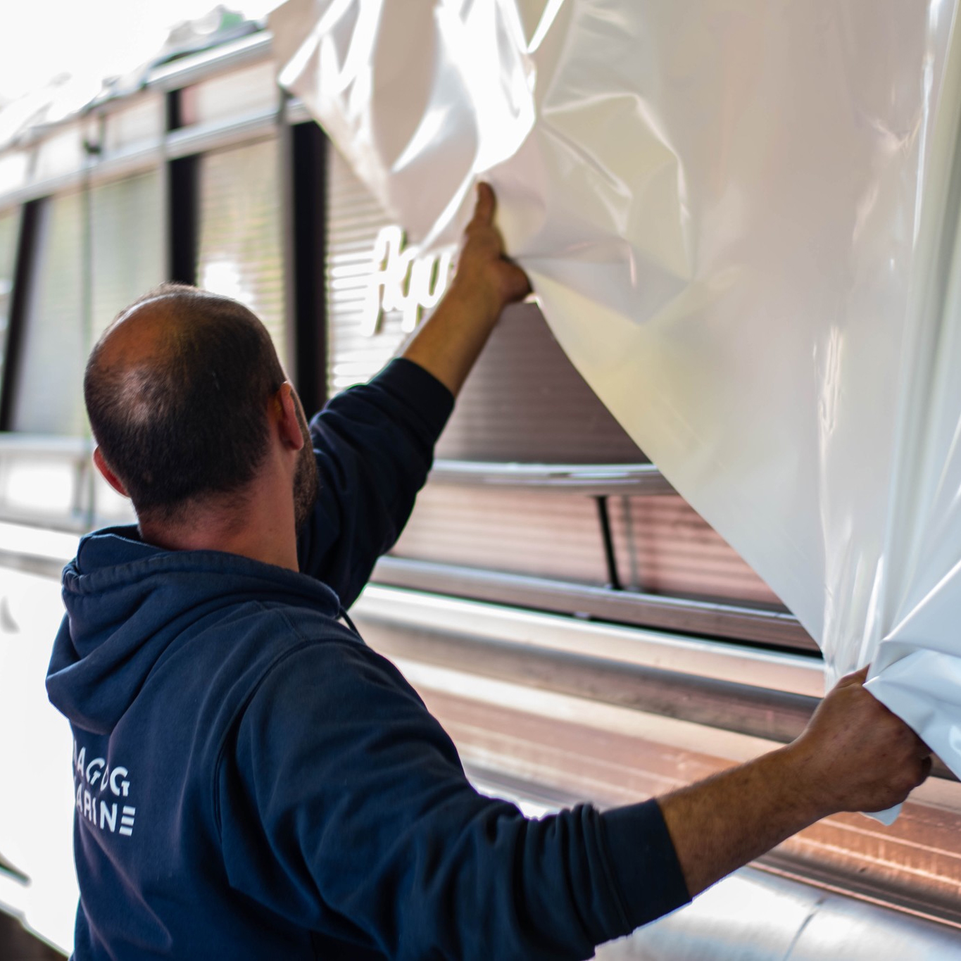 Homme installant une toile de plastique blanche pour la protection hivernale d'un bateau de plaisance